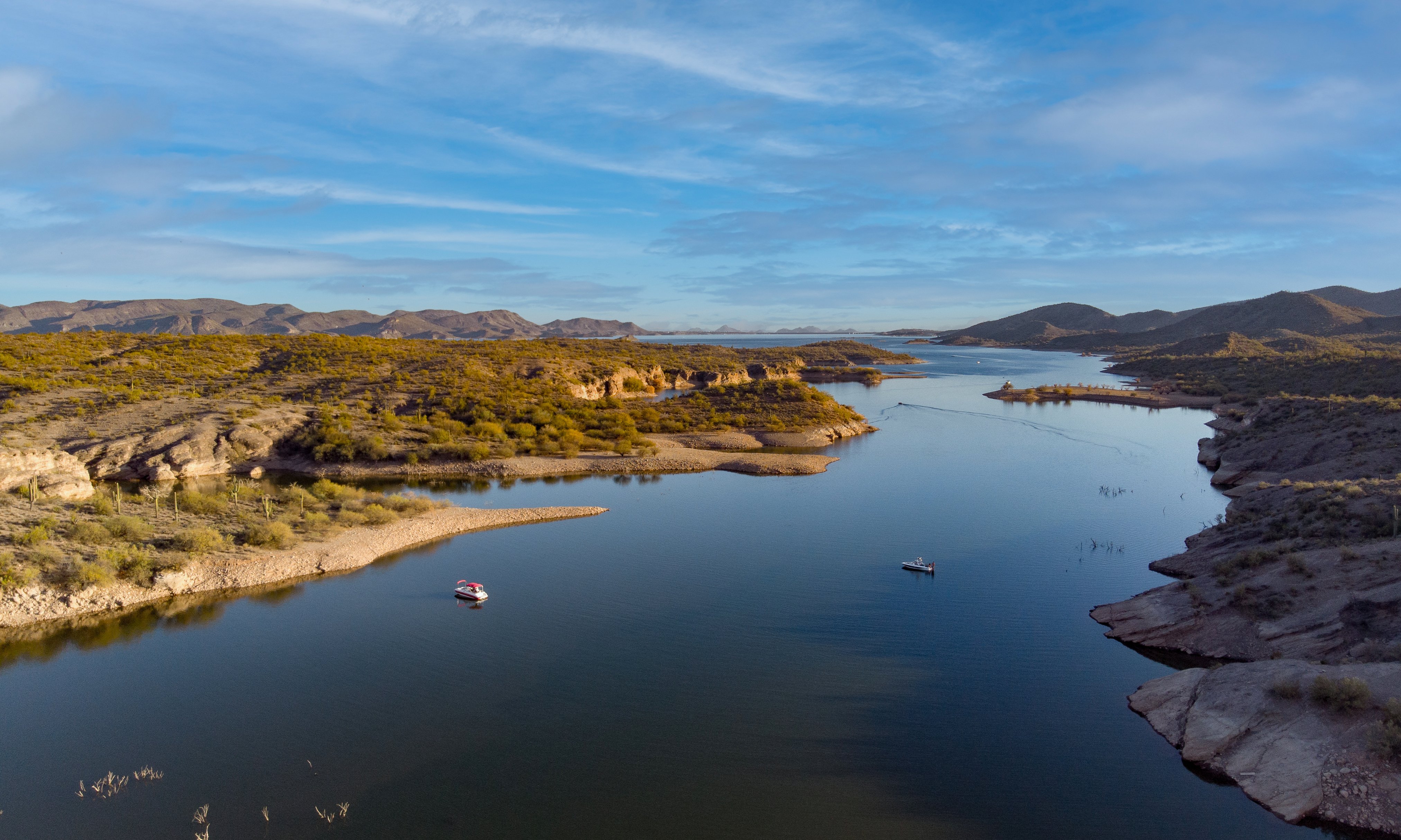 An aerial photo of Lake Pleasant showing serene water, families boating, and a gorgeous mountain backdrop.