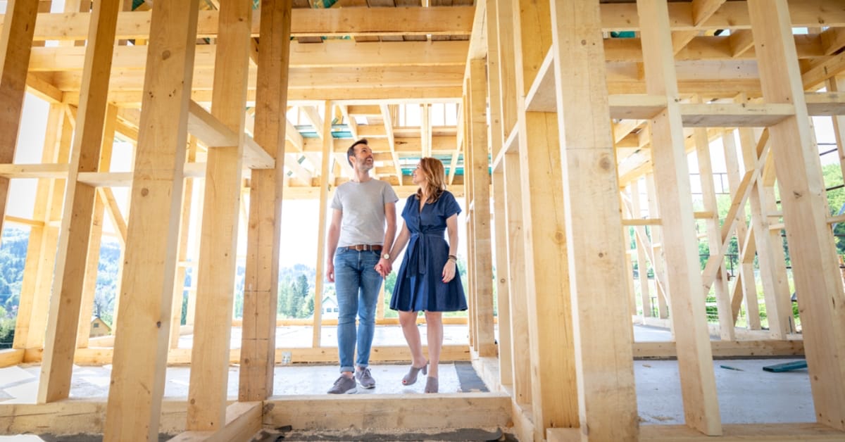 A couple holding hands and walking through their new home under construction.
